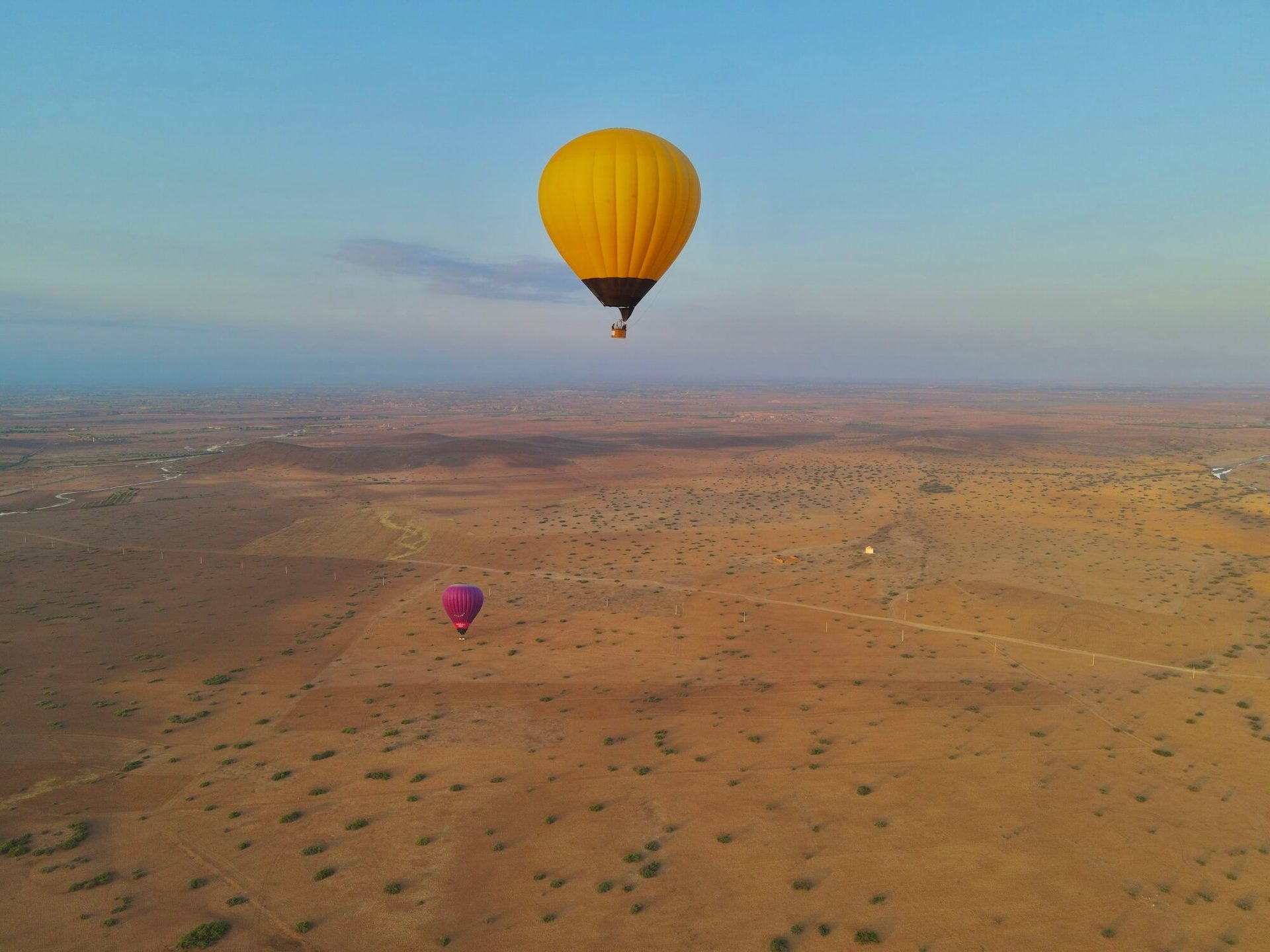 A yellow hot air balloon floating high above the flat land north of Marrakech