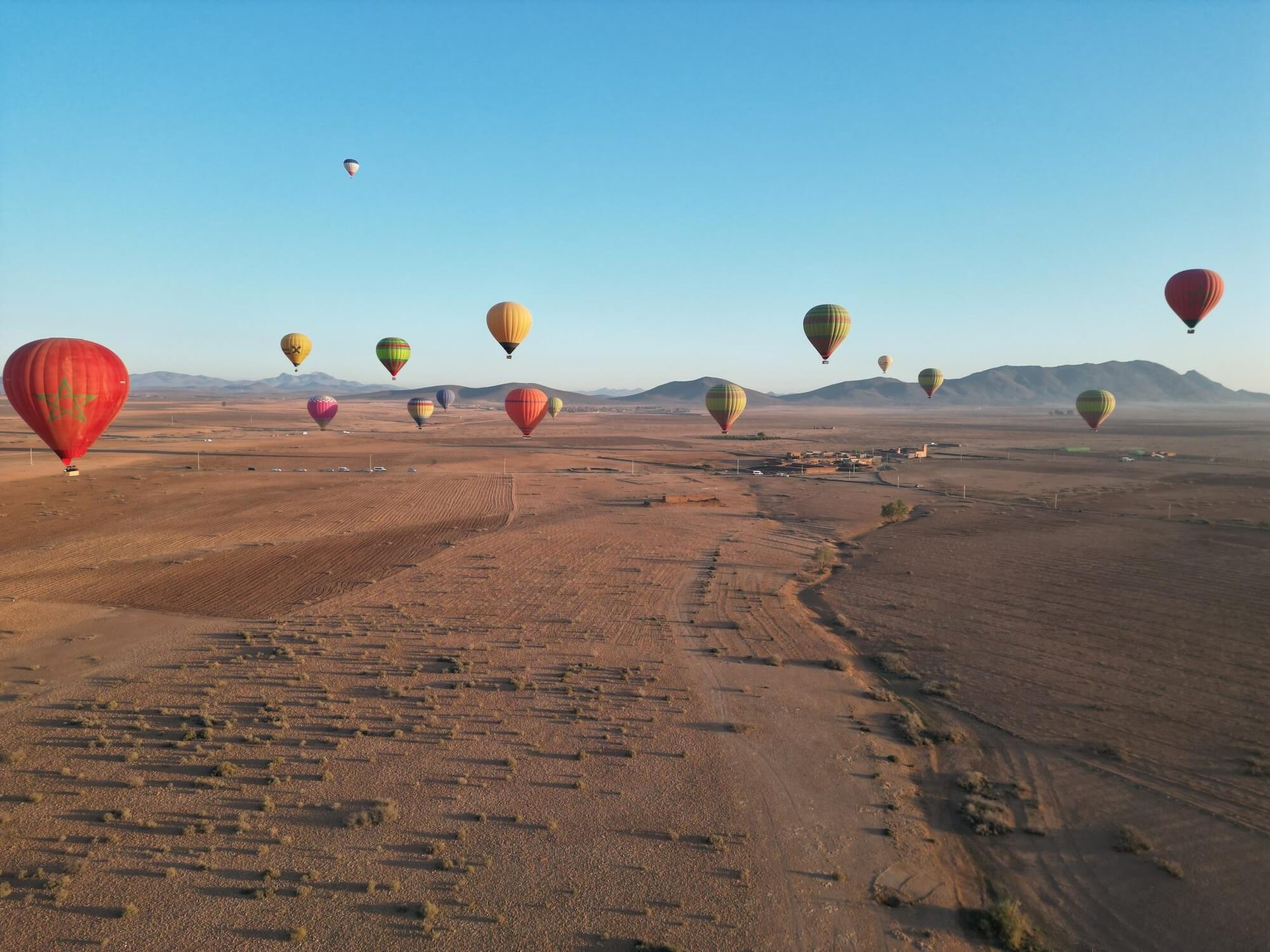 A line of hot air balloons spread across the sky above open desert ground at sunrise